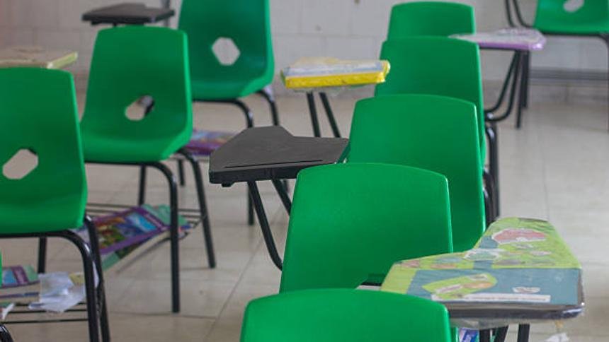 Empty classroom having green chairs and attached desks, ready for students
